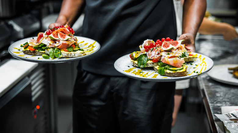 A chef carries two plates of food through a restaurant kitchen