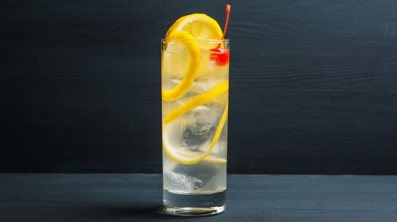 Cocktail in a Collins glass with lemon wedges and a cherry garnish.