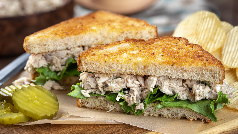 Tuna salad sandwich on toasted bread with pickles and chips