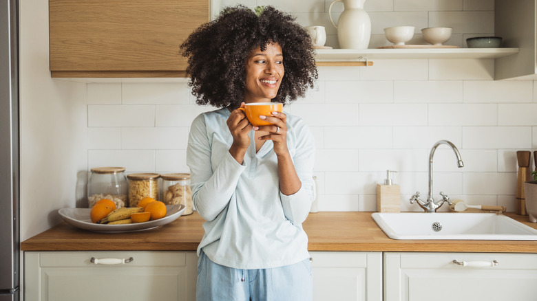 A person in a kitchen holding a large coffee cup
