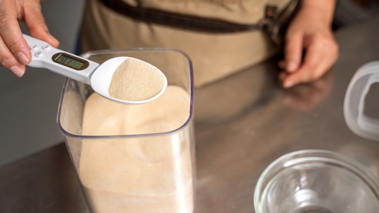 Baker measuring yeast from container with digital measuring spoon near glass bowl