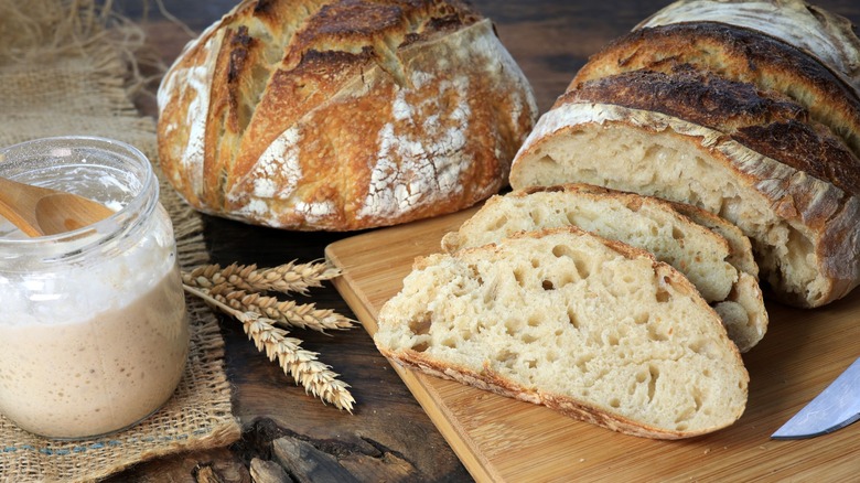 Sourdough bread and slices on wood board with a side of starter in glass jar