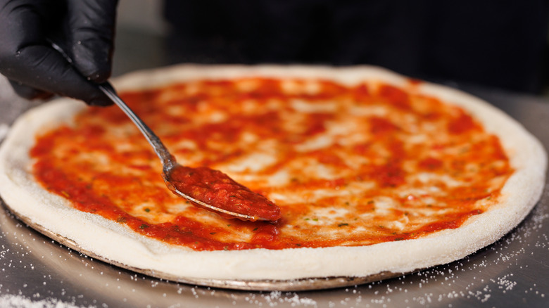 hand spreading pizza sauce over a crust