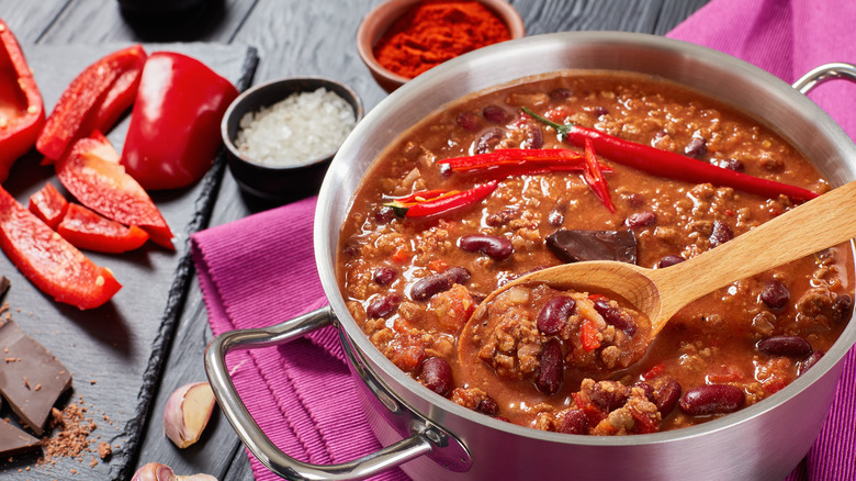 Pot of chili surrounded by peppers and spices.