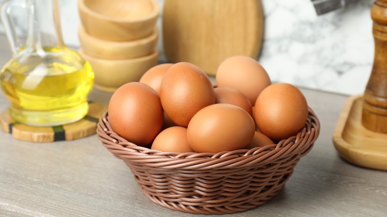 Eggs in a basket, a bottle of oil, and spices on wooden counter.