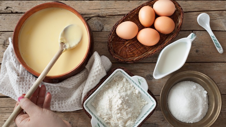 Person stirring custard with egg, flour, cream, and sugar on wood counter