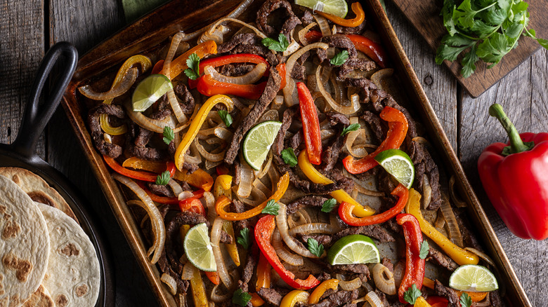 A baking sheet with roasted fajita ingredients next to a skillet with tortillas.