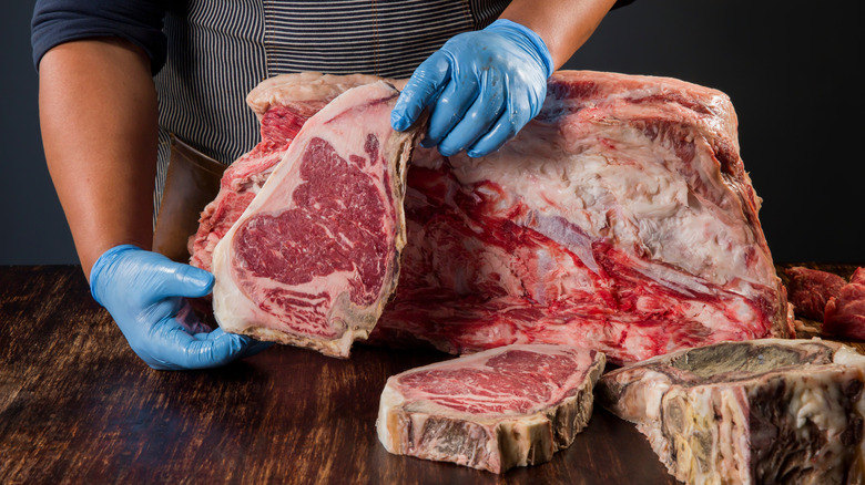 A butcher holding up a thick piece of steak next to a primal cut