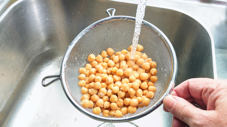 A hand holding a colander of canned beans under running water