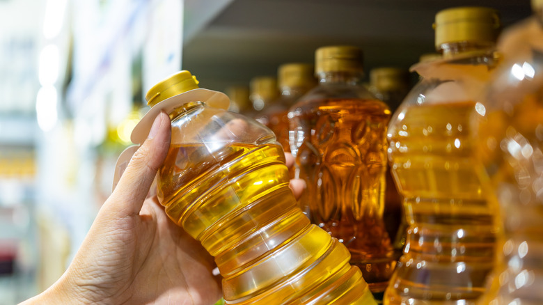 A hand holding a bottle of cooking oil at the grocery store.