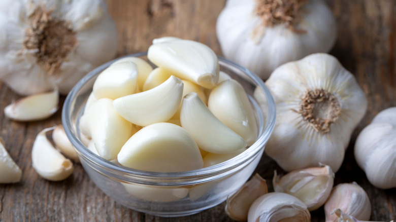 Garlic with peeled cloves in a bowl surrounded by heads of garlic