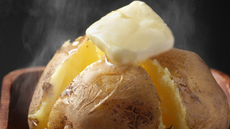 A steaming baked potato, open and topped with butter
