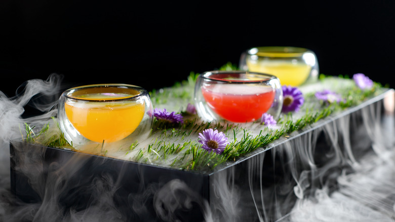 Colorful cocktails in a grassy container with dry ice smoke flowing out