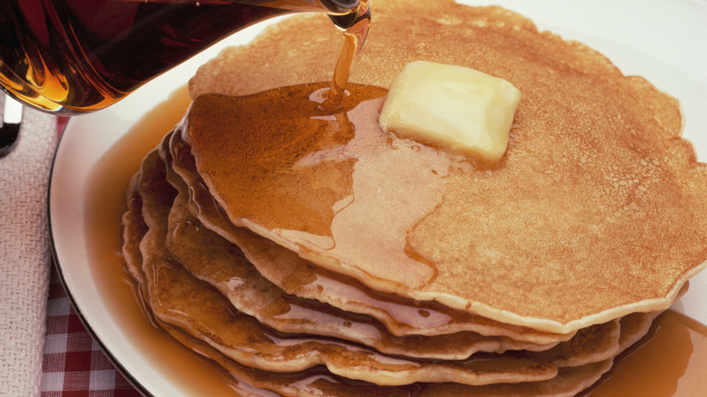Maple syrup being poured on stack of pancakes