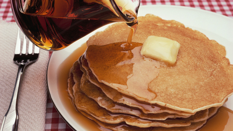 Maple syrup being poured on stack of pancakes