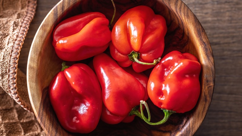 Red habanero peppers in a wooden bowl on a table viewed from above.
