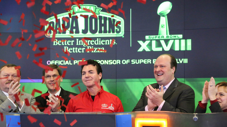 Schnatter, in a red Papa Johns/NFL shirt, stands behind a podium with four executives as red confetti falls.