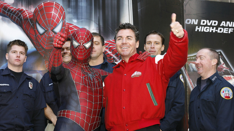 John Schnatter, in a red Papa Johns jacket, stands with Spiderman in front of several first responders. Schnatter and Spiderman give the thumbs-up.