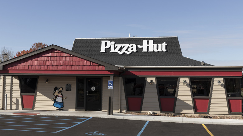 A black and red building with distinctive roof shape and white letters that say Pizza Hut.