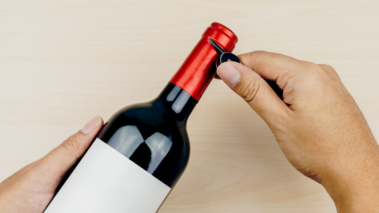 Hand holding corkscrew blade against foil wine capsule