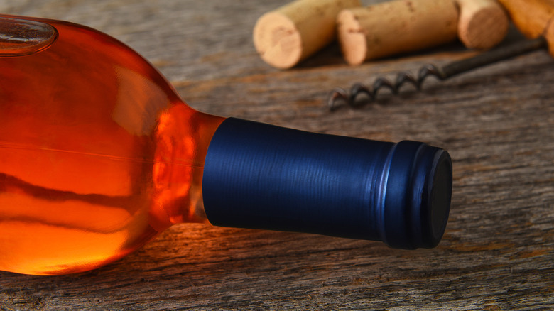Close up on bottle of rose wine with blue foil capsule laying sideways on a wooden surfaces