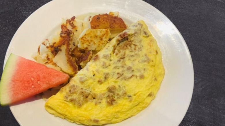 Sausage Omelet with watermelon slice and side of hash browns from House of Omelets on a white plate