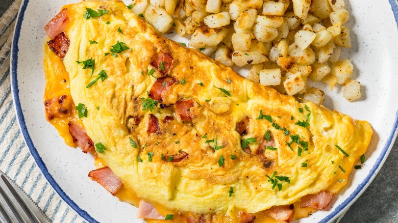 Homemade Ham and Cheese Omelette with Potatoes for Breakfast on a white plate with a blue rim