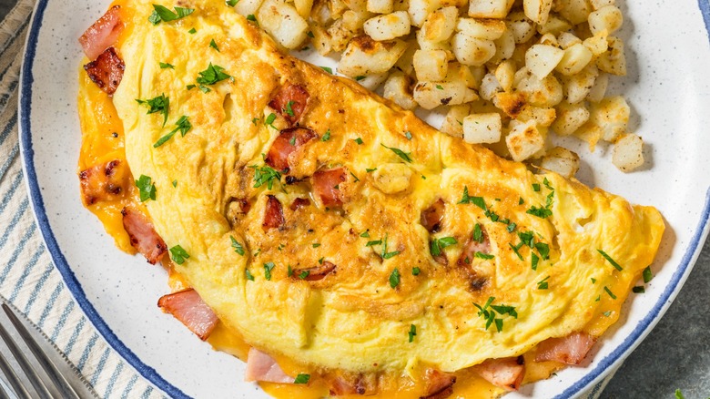 Homemade Ham and Cheese Omelette with Potatoes on a rustic white plate with a blue rim