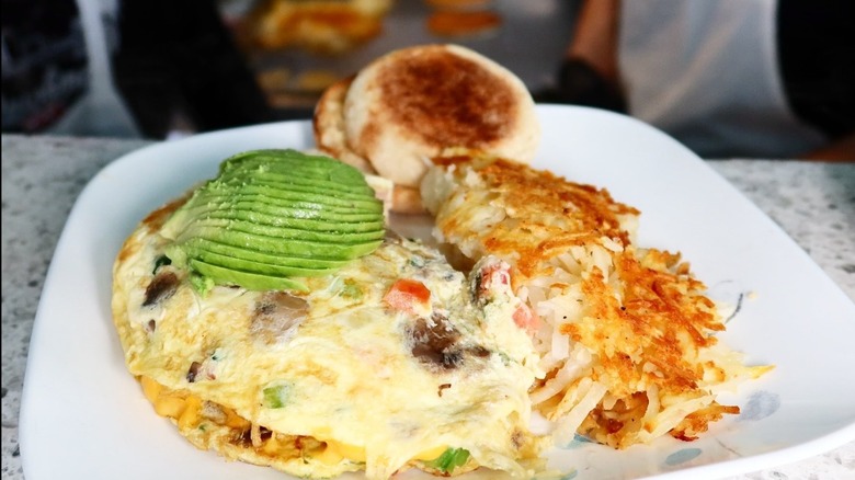 Omelet topped with avocado with side of hash browns and English muffin from Whistle Stop Diner - Pleasant Ridge on a white plate