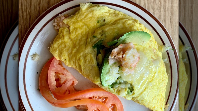 Omelet with avocado and fresh slice of tomato on the side from the Omelet House on a white plate with a brown striped rim
