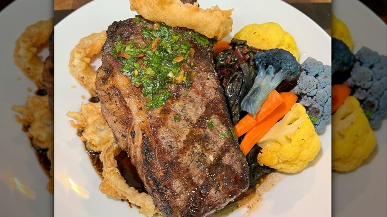 steak with multicolored cauliflower, onion sirngs, and carrots