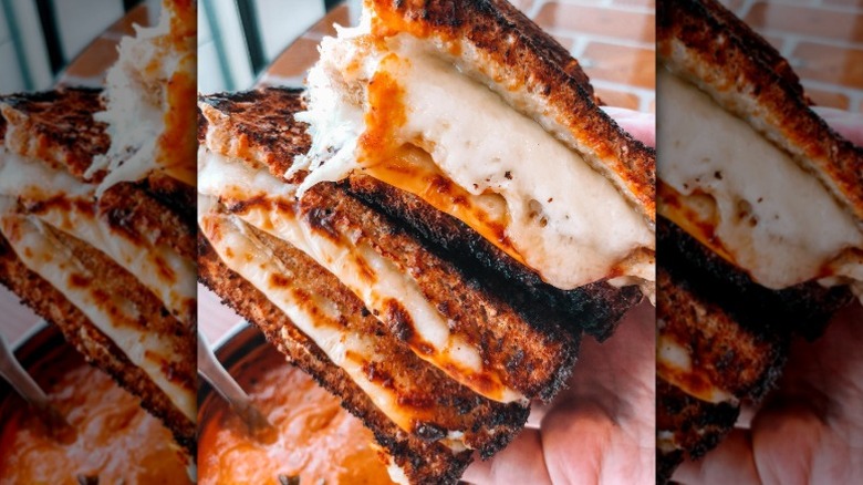 Hand holding a grilled cheese with Vermont cheddar, Swiss and American Cheese, with a side of tomato bisque