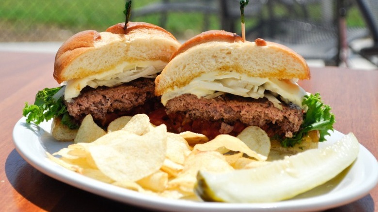 cross section of a burger with cheese and lettuce, with a side of chips and a pickle