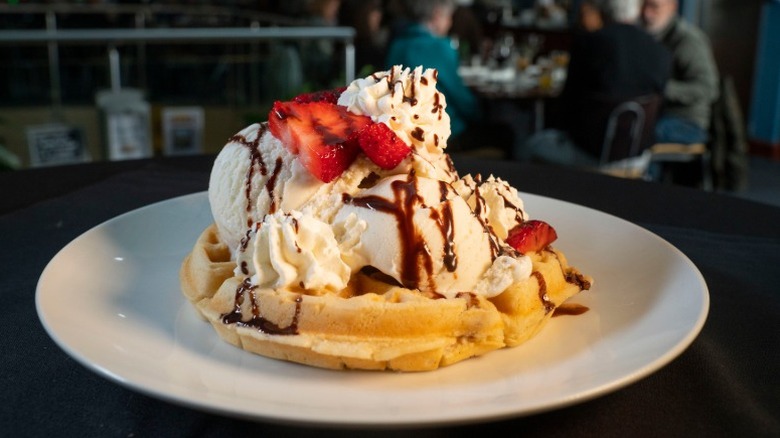 waffle topped with scoops of vanilla ice cream, whipped cream, chocolate sauce, and strawberries