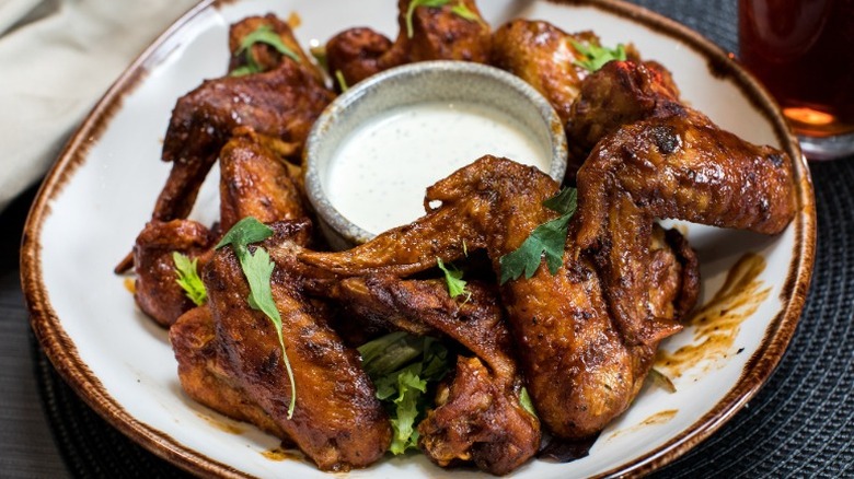 chicken wings with green garnish arranged on a plate around a cup of ranch