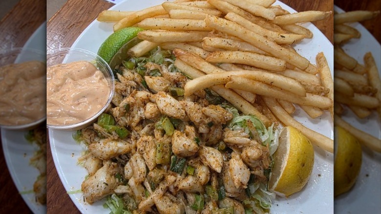 fish with vegetables, a side of fries, sauce, and lemon and lime wedges
