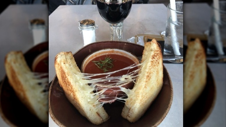 halved grilled cheese on a plate with a bowl of tomato basil soup and a glass of wine