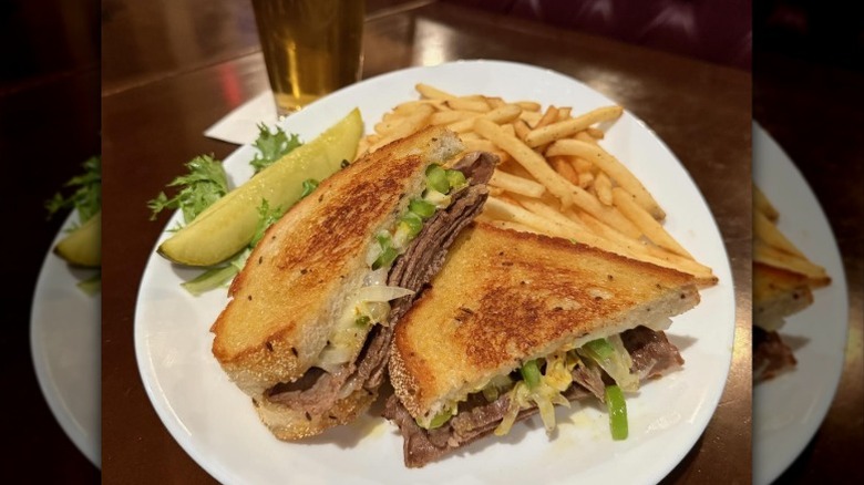 a sandwich with roast beef, onions and peppers, and cheese on rye bread with a side of fries and a pickle