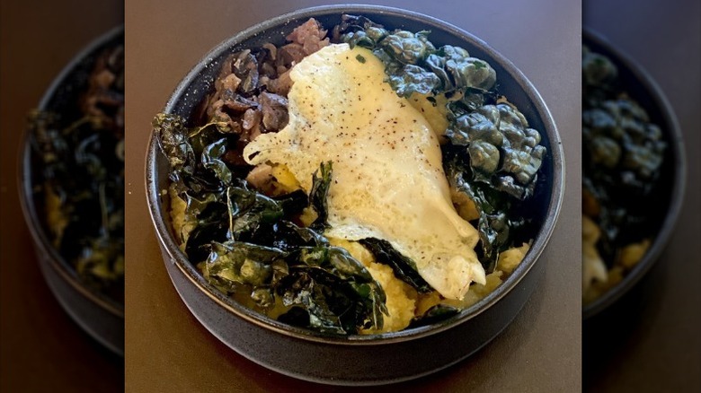 a bowl of polenta with greens, meat, and a fried egg