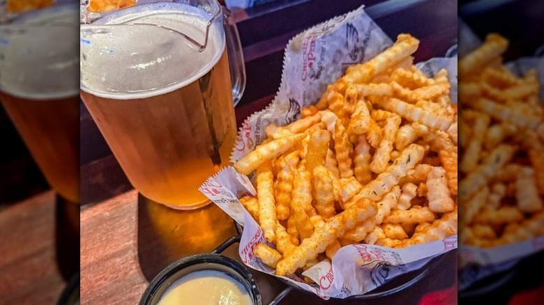 a basket of crab fries with sauce and a pitcher of beer on the side