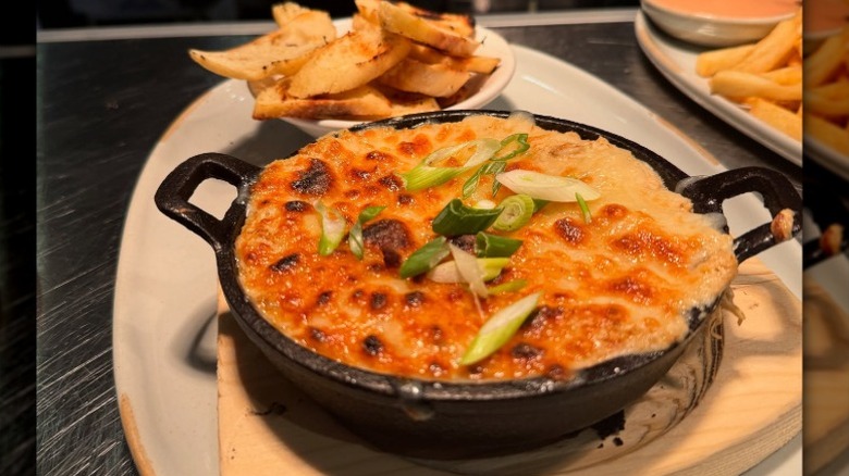 a skillet topped with bubbling melted cheese and green onions with a side of toasted bread