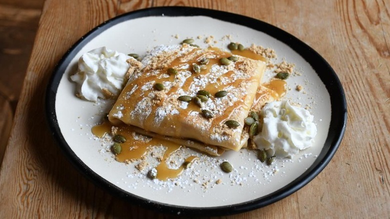 crepe with powdered sugar, whipped cream, caramel sauce, and pumpkin seeds on a plate