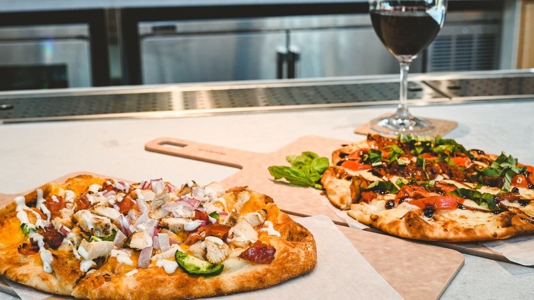 Two pizzas on wood serving padels with a glass of red wine behind