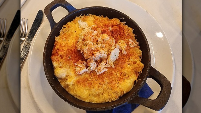a cast iron skillet with baked mac and cheese with bread crumbs and seafood on top sits on a plate