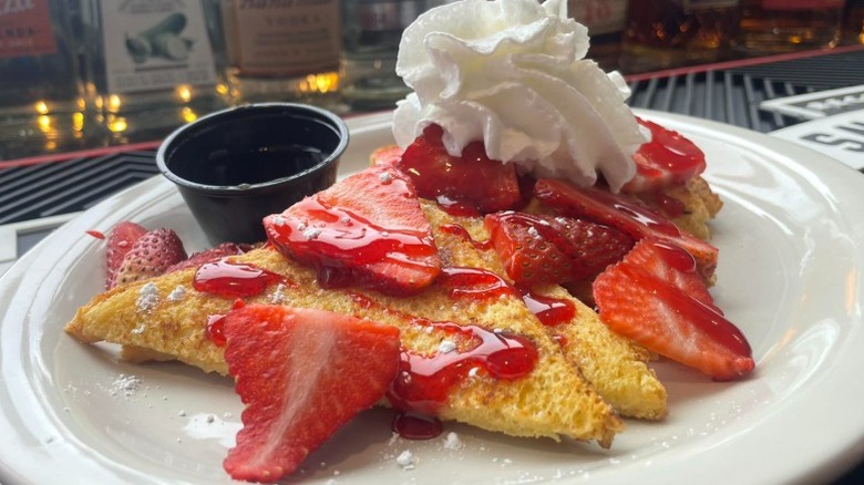 french toast with strawberries, strawberry syrup, powdered sugar, and whipped cream on a plate