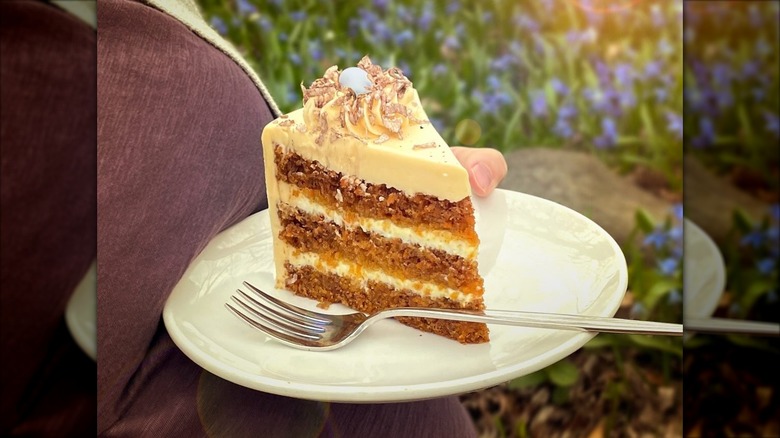Hand holding plate with slice of layered cake and fork