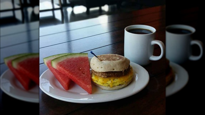 A delicious biscuit breakfast sandwich with two slices of watermelon and a cup of coffee
