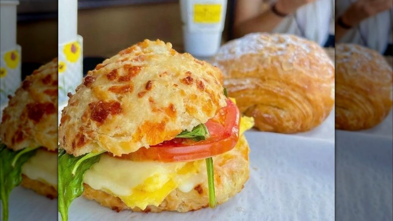 A biscuit sandwich with egg and tomato with a croissant in the background