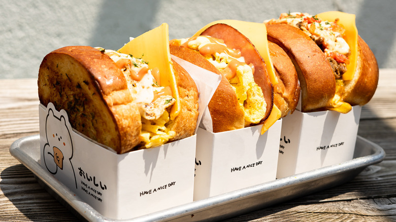 Three breakfast sandwiches with egg peaking out the top of grilled bread in boxes