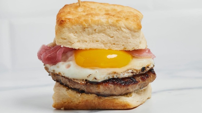 A biscuit sandwich with egg, sausage, and pickled onions